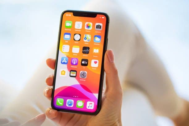 Hand holding an iPhone showing its home screen